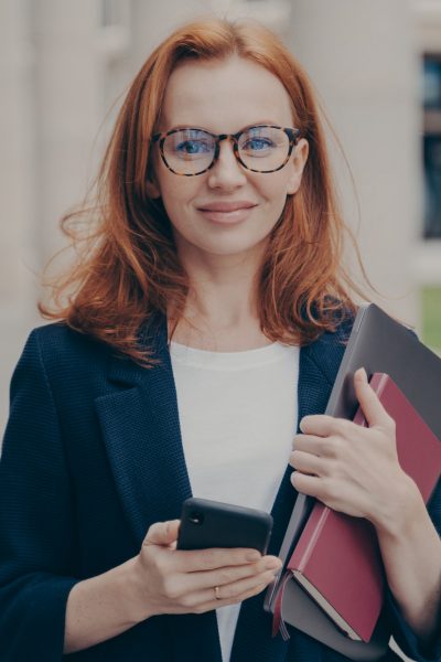 confident-beautiful-red-haired-female-business-consultant-holding-modern-smartphone-and-laptop.jpg